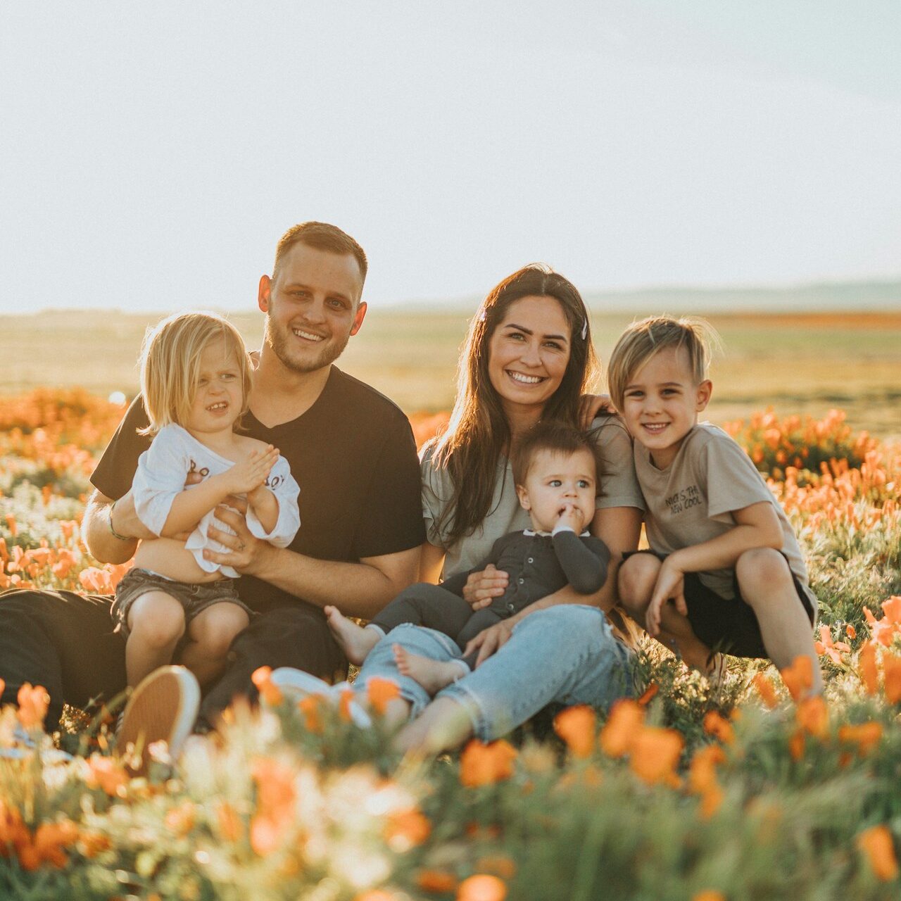 family with 3 young children sat on grass with orange flowers